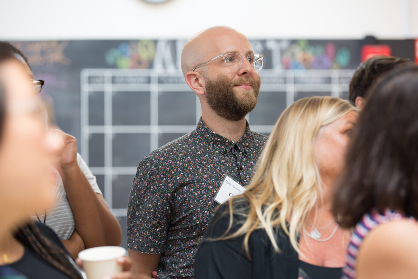 Man standing amongst other people out of focus. Listening to someone out of frame.