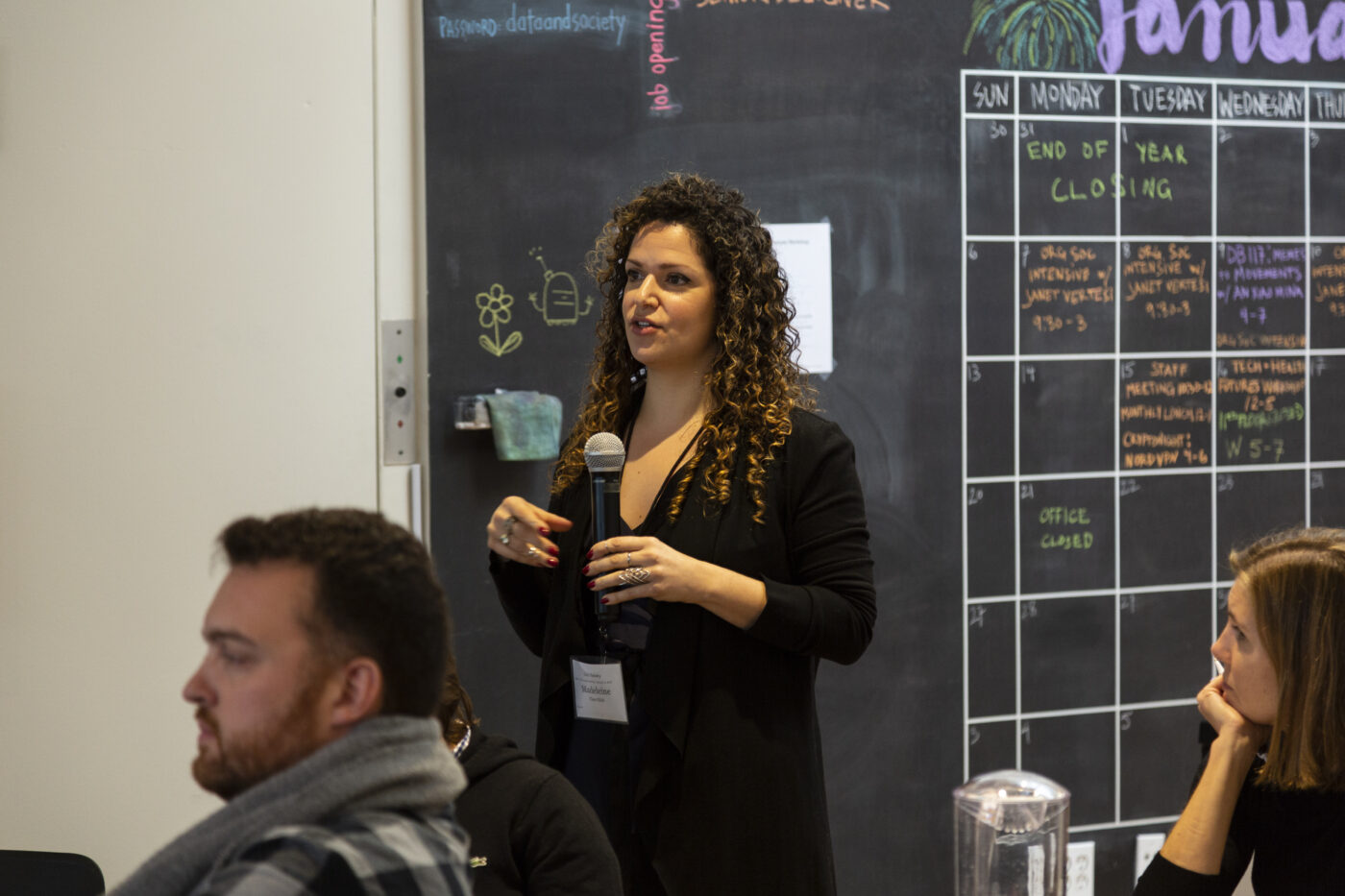 Woman with microphone asking question of presenter, two seated people are nearby