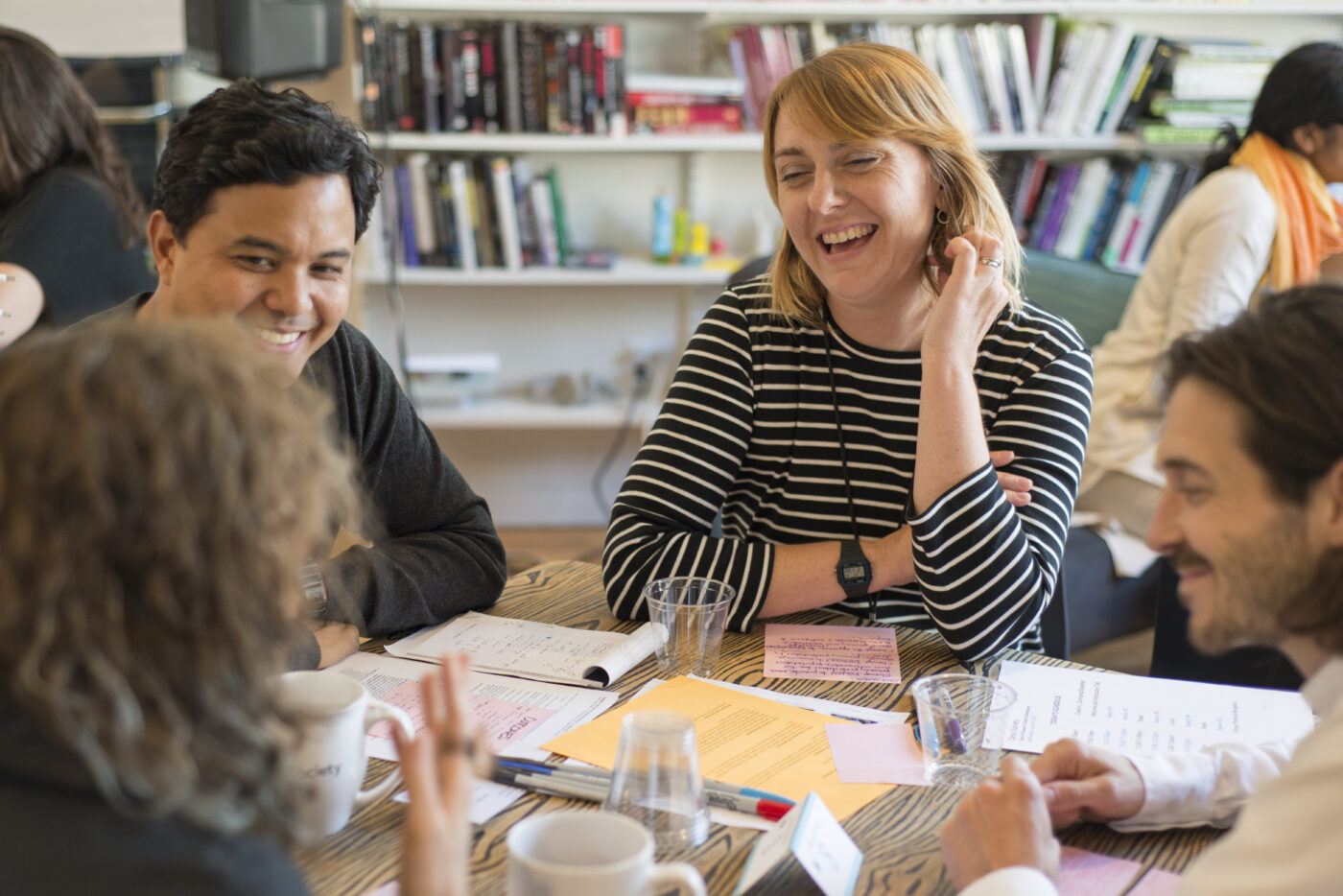 Four people sitting at a table, laughing with person whose back is facing the camera.