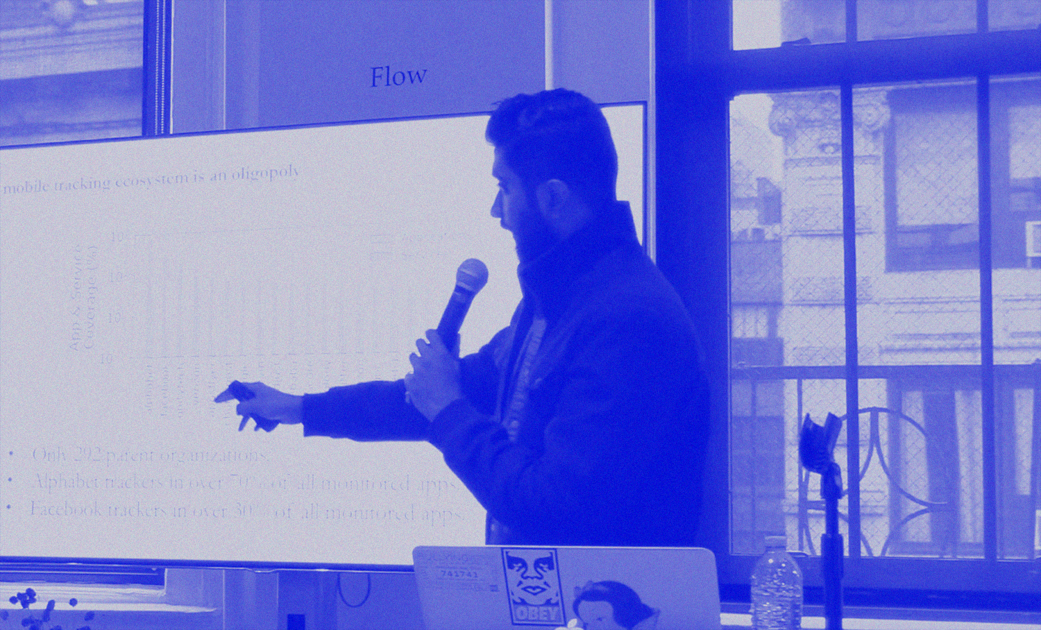 man holding microphone and pointing at his presentation on the monitor next to him