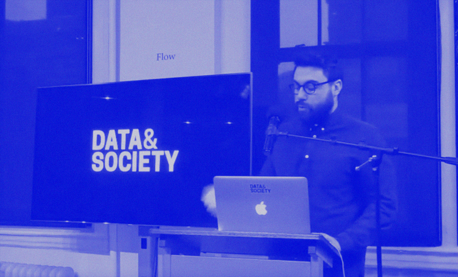 photo of person with facial hair and glasses presenting in front of screen that says 